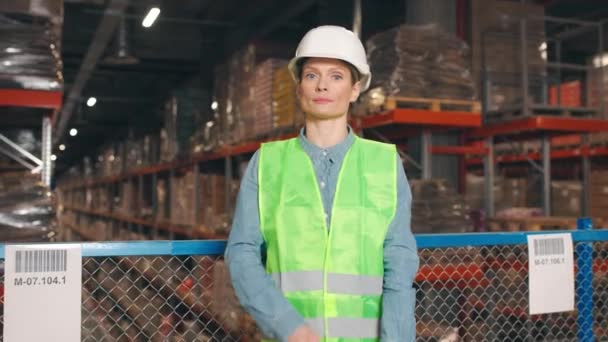 貯蔵橋に立っている女性の笑顔の従業員 保護堅く 反射のジャケットの倉庫の労働者 クロスアームでカメラを見ている女性請負業者 ロジスティック企業 — ストック動画