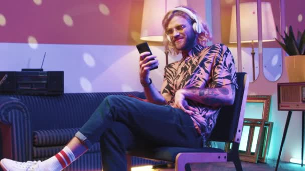 수평한 힙스터 앉아서 휴대폰을 디스코 스타일의 방에서 헤드폰을 음악을 빈티지 — 비디오