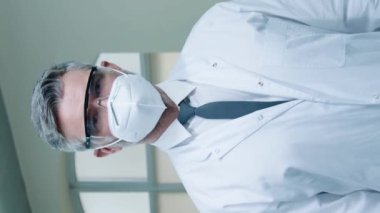Kameraya bakarken gözlüklü ve solunum cihazlı beyaz önlüklü erkek bilim adamının portresi. El ele tutuşup laboratuvar odasında dikiliyoruz. Geliştirme merkezinde çalışıyorum. Hastane kavramı.