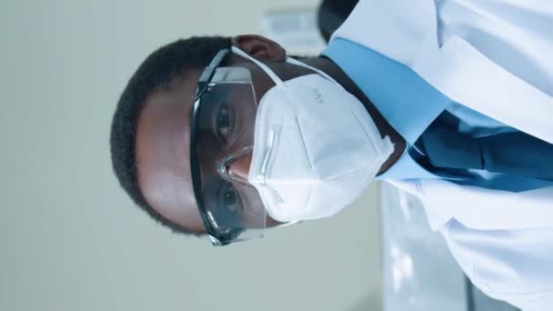 近代研究所で働くアフリカ系アメリカ人の男性生化学者の肖像画と ウイルスからの医薬品やワクチンの探索 顕微鏡を使用している間保護装置を身に着けている勤勉な男 — ストック動画