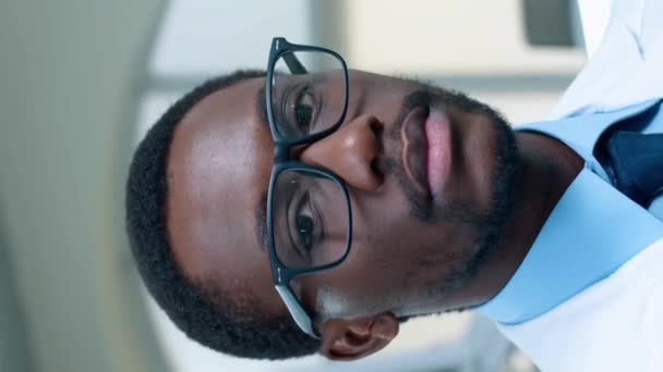 ハンサムなアフリカ系アメリカ人の医師の垂直方向は カメラで喜びを見つけるためのより良いビジョンを身に着けています 医療センターにおける患者の治療 科学を開発する 医療コンセプト — ストック動画