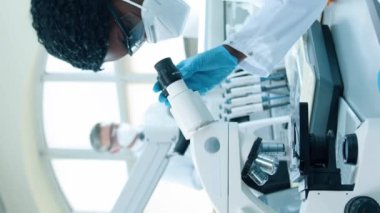 Modern tıp laboratuarında çalışan Afrikalı Amerikalı kadın mikrobiyolog ya da Google ve koruyucu laboratuvar önlüklü bilim adamı. Mikroskop altında ilaç veya kan örnekleri inceleniyor.