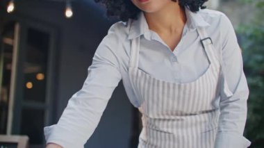 Mavi gömlekli ve önlüklü Afro-Amerikalı çekici bayan barista sabahları tek başına kafe terasında çalışıyor. Bakteri beziyle masaları temizliyorum. Müşteri kabul etmeye hazırlanılıyor.