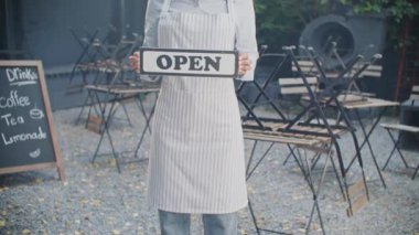 Afro-Amerikalı kadının elinde açık şarkı söylerken kameraya bakması. Kıvırcık bayan garson rahat bir sokak terasında duruyor ve müşterileri bekliyor. Kafe konseptinde çalışmak.