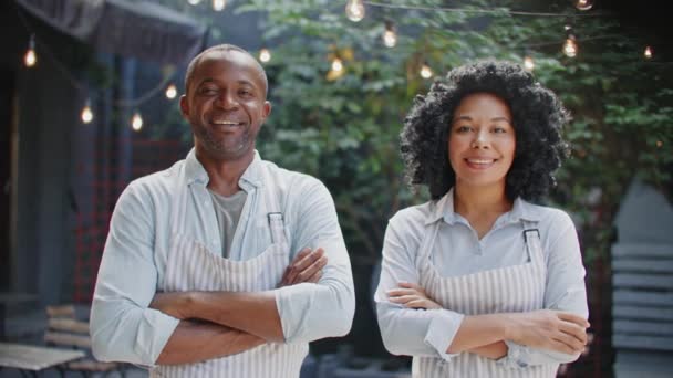 2人のアフリカ系アメリカ人労働者が カメラの前に立っている間に手を横切っている ポジティブな人々は 現代のカフェで働いている間に喜んで微笑んでいます パートナーシップ コワーカーのコンセプト — ストック動画