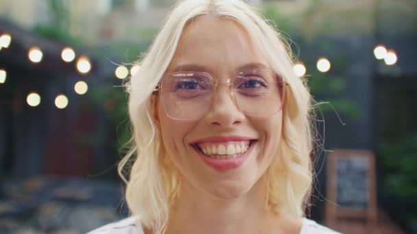 白种人女人在镜头前喜笑颜开的画像 戴眼镜的快乐女士站在街上的咖啡店前 目光远大 在舒适的阳台上休息后有良好的感觉 — 图库视频影像