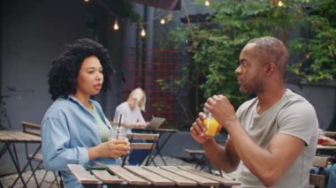 Kafedeki masada oturan güzel Afro-Amerikan çiftin yan görüntüsü. Kıvırcık kadın güzel erkeğiyle konuşuyor. İnsanlar güneşli yaz gününde taze kokteyller içiyor. Hafta sonları birlikte dinleniyoruz..