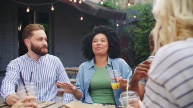 Bir grup melez insan açık hava kafeteryasında masada otururken konuşuyor. Mutlu arkadaşlar terasta lezzetli kokteyller içerken konuşuyor. Komik bir konuşma. İletişim konsepti.