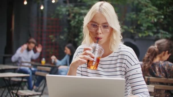 美丽的白种人女人 金发碧眼 喝了一小口 喝了一大杯最喜欢的饮料 一边吃一边看笔记本电脑 考虑下一个项目 在餐馆享受闲暇时光 — 图库视频影像