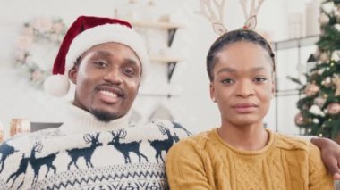 Kanepede oturan örgü kazak giyen Afro-Amerikan evli çiftin portresi. Noel Baba şapkalı çekici bir adam. Geyik boynuzlarıyla güzel karısına sarılıyor. Noel ruhu.