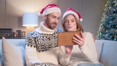Kocasıyla birlikte güzel bir kadın Noel için tablet cihazından hediye seçiyor ya da çocukları ya da akrabaları için yeni yıl hediyesi. Noel Baba şapkalı mutlu aile tatili kutlamaya hazırlanıyor..