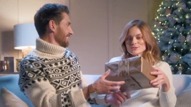 Yakışıklı beyaz adam, sevgili karısına Noel hediyesi veriyor. Mutlu kadın şaşkınlıkla hediyeye bakarken sevinçle gülümsüyor. Noel 'i evde kutlayan bir aile. Kış tatili kavramı.