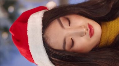 Noel Baba şapkalı Asyalı kız portresi Noel hediyesi alıyor. Kırmızı dudaklı genç bir kadın parıldayan paketi açarken şaşkınlıkla hediyeye bakıyor. Tatil için hediye alıyorum. Kutlama etkinliği.