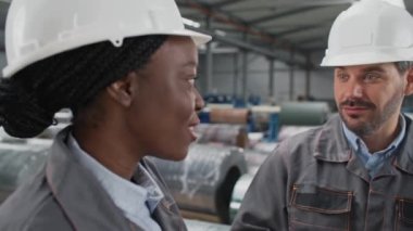 İmalat fabrikasındaki ustabaşıyla konuşan genç bir kadının yan görüntüsü. Sakallı adam iş arkadaşına şaşkınlıkla bakıyor. İnsanlar içeride sohbet ediyorlar. İletişim konsepti.