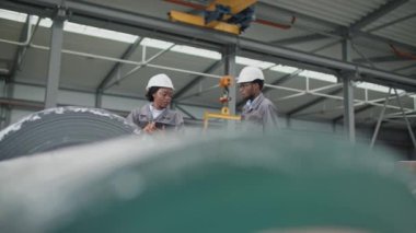 Afrikalı Amerikalı işçiler fabrikadaki üretim sanayi ürünlerinin miktarını kontrol ediyorlar. Tablet cihazını tutan ve atölyedeki yakışıklı meslektaşıyla yürüyen genç bir kadın. Takım çalışması