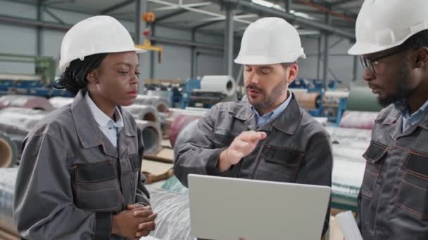 산업용 제품을 저장하는 창고에 서있는 헬멧과 제복을 이야기하는 노동자 동료와 — 비디오