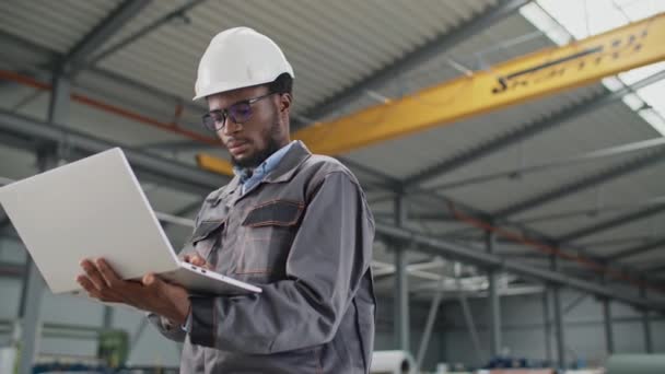Серьезный Афроамериканский Инженер Использующий Ноутбук Рабочем Месте Рабочий Шлеме Униформе — стоковое видео