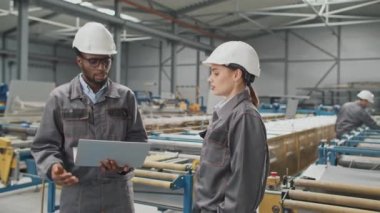 İyi görünümlü çok ırklı insanlar depoda sohbet ediyorlar. Çekici ustabaşı portatif laptop tutarken güzel bir kadınla konuşuyor. Atölyede imalat hakkında konuşmak.
