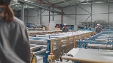 Üniforma giyen melez insanlar büyük fabrikada çalışıyor. Güzel bir kadın üretim bandının arasında yürürken telefonla konuşuyor. İşçiler üretim sürecini kontrol ediyor.