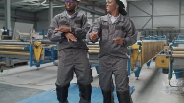 Üniformalı ve kasklı iki Afrikalı Amerikalı işçi depoda ya da fabrikada eğleniyor. Tesiste üretim sırasında mutlu insanlar birlikte dans ediyor. Eğlence konsepti.