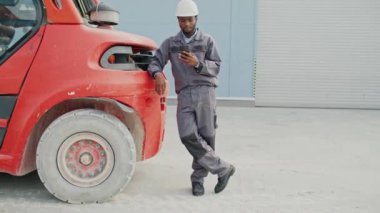 Üniformalı ve güvenlik teçhizatlı Afro-Amerikan işçilere yaklaşmak kamyonun yanında ya da dışarıda durmak. Genç adam akıllı telefonunu kullanıyor ve kameraya gülümsüyor..