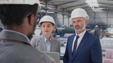 Üniformalı bir işçinin depodaki iki yakışıklı yöneticiyle konuşmasının arka görüntüsü. Başarılı bir adam ve güzel bir kadın iş saatleri hakkında konuşurken dizüstü bilgisayar kullanıyorlar..