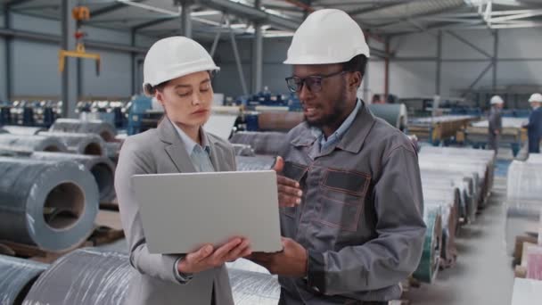 英俊的工头 穿着工作服 头戴安全帽 向漂亮的经理解释一些事情 年轻的女士拿着手提电脑 积极地倾听工人们的声音 工业制造业 讲习班 — 图库视频影像