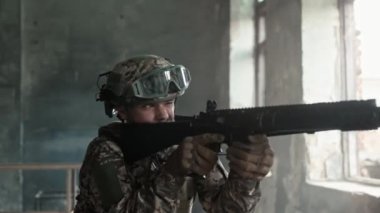 Camdan içeri silah doğrultmuş kamuflajlı bir savaşçı. Cesur asker savaşa hazırlanıyor. Düşmana ateş etmek. Terk edilmiş binada saklanmak. Muhalefete hazırız. Savaş kavramı.