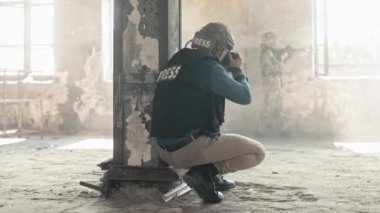 Terk edilmiş bir binada bombardımandan saklanan askerlerin kamera önünde fotoğraf çeken muhabirin dikiz görüntüsü. Askeri bir kavram. Çatışma sırasında güvenlik kaskı ve kurşun geçirmez yelek giyen insanlar