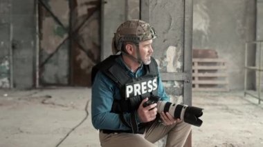Koruyucu ekipman içinde askeri foto muhabiri terk edilmiş binada kamerayla fotoğraf çekiyor. Beyaz adam savaş bölgesinde harabelerin fotoğrafını çekiyor. Tehlikeli bir iş. Askeri çatışma sırasında kitle iletişim araçları.