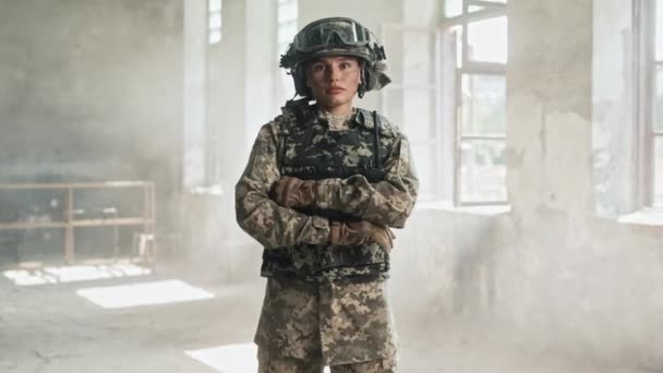 美しい白人女性兵士が軍服と安全装備を着てカメラを真剣に見ている 見捨てられた建物に立っている勇敢な女性戦士 — ストック動画