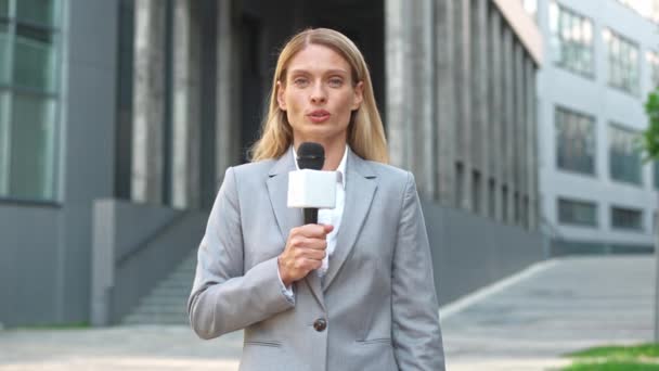 严肃的白人女记者穿着灰色服装在镜头前与话筒交谈 一个忙着为电视频道播报新闻的女人 喜欢在电视媒体工作 相应的概念 — 图库视频影像