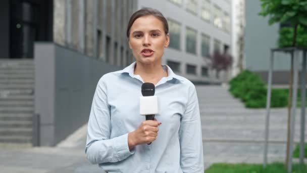 年轻的专业白人记者穿着蓝色T恤站在街上报道城镇的真实新闻 美丽的阿哈尔一边拿着话筒一边对着摄像机说话 直播节目 — 图库视频影像