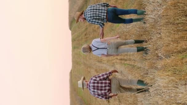 マウドフィールドを横断する農民の家族の背後にある景色 祖父は息子と孫と話し プランテーションに時間を費やしている 人々はお互いに話し合っている 農業事業について — ストック動画