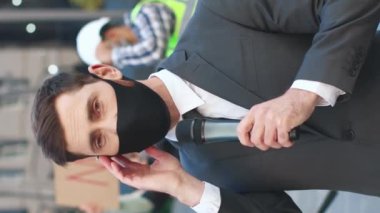Dikey çekim. TV haberleri için koruyucu maske takan erkek hoparlörden canlı yayındayız. Gazetecinin mikrofonuyla ciddi bir konuşma. Öğrenciler ve işçi sınıfı çalışanları. Aşıya karşı Avrupa protestosu
