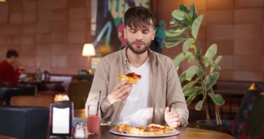Kafedeki masada oturan yakışıklı sakallı adam. Lezzetli İtalyan pizzası yiyen aç bir erkek. Bir parça iştah açıcı yemek ve ısırık. Genç adam fast food seviyor. Modern restoran.