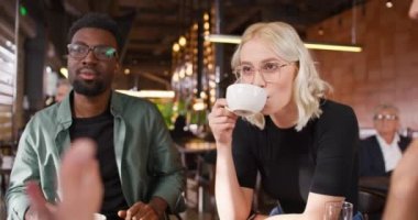 Kafedeki masada yan yana oturan melez dostların kamera görüntüsü. Aktif olarak konuşuyorlar ve mutlu bir şekilde gülümsüyorlar. Olumlu konuşuyorlar. İnsanlar hafta sonları barda dinleniyorlar..