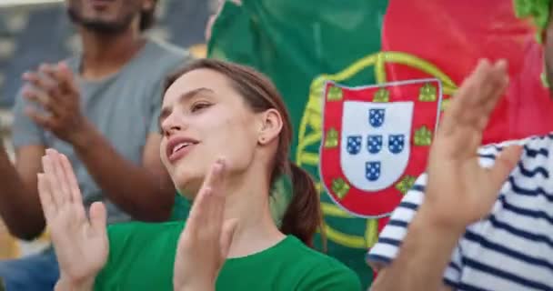 スポーツトーナメントを見ながらポニーテールヘアの美しい女性 ポルトガル国旗を持ったファンが女の子に何かを叫ぶ お気に入りの選手を応援する人 — ストック動画