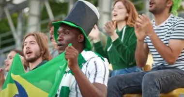 Tribünlerde otururken elinde Brezilya bayrağı tutan çok ırklı insanların görüntüsü. Hayranlar ellerini çırpıyor ve oyuncuların zaferi için sloganlar atıyorlar. Yumurtlama. Spor eğlence konsepti.