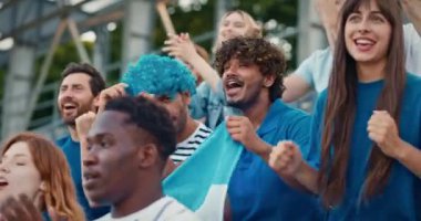 Tribünlerde spor şampiyonası izleyen melez bir kalabalık. İnsanlar aktif olarak takımları destekliyor. Arjantin bayrağı tutan ve maç boyunca tezahürat yapan dost canlısı taraftarlar. Canlı oyun.