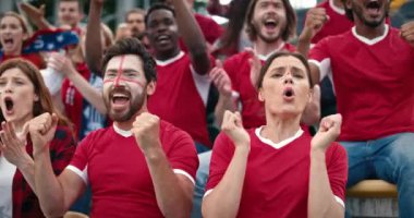 Kırmızı tişörtlü güzel hayranlar tribünde oturuyor. İnsanlar futbol maçı izliyor ve oyunculara tezahürat yapıyor. Spor müsabakalarında vakit geçirmekten zevk alıyorum. Kazanan şampiyonluk.