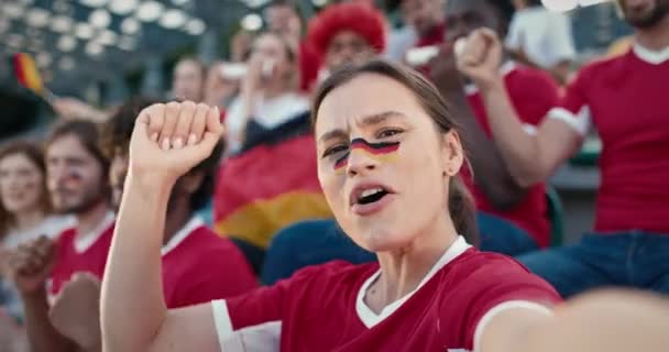 美しい白人女性がカメラを保持し スポーツイベントで何かを叫んで自分自身を記録します ドイツ国旗を掲げた女性が顔に描かれている チームをサポートしながら素晴らしい時間を過ごす — ストック動画
