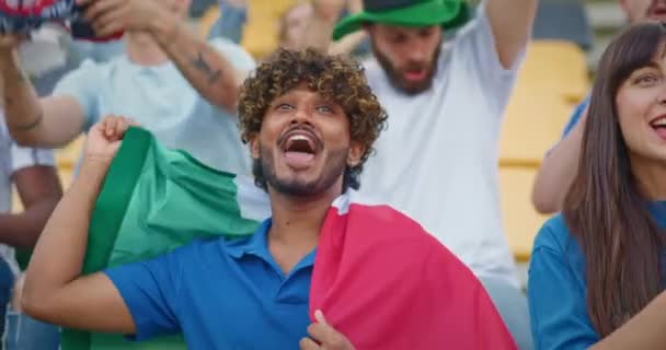 スポーツトーナメント中にイタリア国旗を掲げるハンサムな男 若者は積極的にチームを応援している 歌を歌ったり サポートの言葉を叫んだり チャンピオンシップ中に楽しんでいるハッピーファン — ストック動画