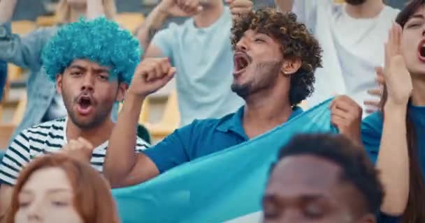 在与多种族人群坐在讲台上的时候 积极的球迷们支持来自阿根廷的球队 在运动会期间 情绪激动的男人举着国旗唱歌 娱乐的概念 — 图库视频影像