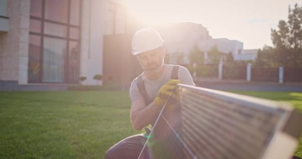 再生可能エネルギー企業で働いている白人男性 芝生の専門の請負業者は王冠をかぶっています 太陽電池パネルを設置する男性技術者 電気への日光の変換 — ストック動画