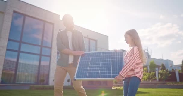父亲和女儿面带微笑 带着替代能源 快乐的父亲和女儿牵着太阳能电池板 男人和女孩在外面安装可再生能源系统 生态意识 — 图库视频影像