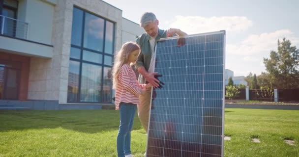 父亲和女儿解释了保护地球生态系统的重要性 父亲和女儿在太阳能电池板附近外面草坪上的男人和女人将阳光转化为电 — 图库视频影像