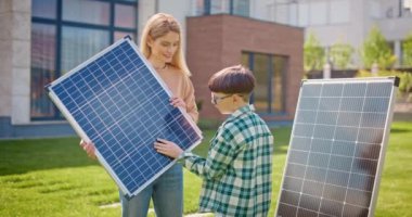 Anne güneş panelini tutuyor ve oğluyla konuşuyor. Anne ve oğlu güneş panellerinin yanında. Küçük çocuk dikkatlice güneş paneline bakıyor. Güneş ışığının elektriğe dönüştürülmesi. Çevre bilinci kavramı.