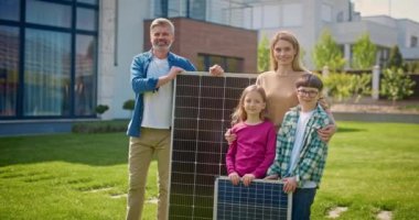 Mutlu aile güneş panellerinin yakınındaki kameraya bakıyor. Modern evin arka planında gülümseyen aileler ve çocuklar. Güneş panelleriyle çimlerde poz veren neşeli bir aile. Çevre bilinci kavramı.