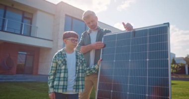 Babam güneş panelini tutuyor ve oğluyla konuşuyor. Baba ve oğul güneş panellerinin yanında. Küçük kız dikkatlice güneş paneline bakıyor. Güneş ışığının elektriğe dönüştürülmesi. Çevre bilinci kavramı.